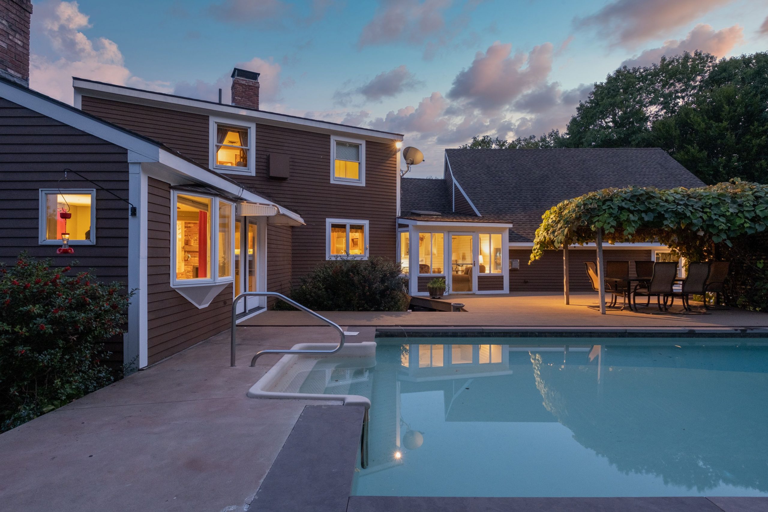 A modern cozy lit house and a pool under a cloudy sky in the evening